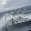 風が強い日のジギングで船が揺れ、波しぶきが上がる船首の様子