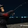 猿の面と帽子をかぶった釣り人が太刀魚ワインドのしゃくりをして肘に負担がかかっている様子